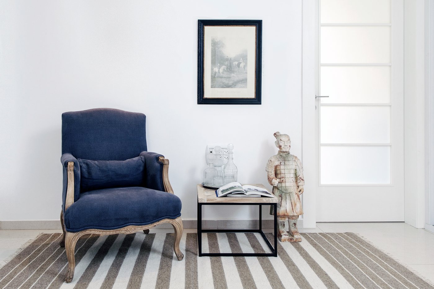 A transitional living room vignette anchored by a French blue armchair and a striped rug.